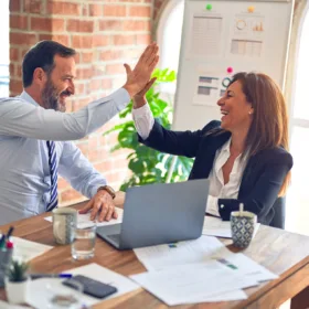 Due colleghi di lavoro, un uomo e una donna, si danno il cinque felici, seduti in un ufficio